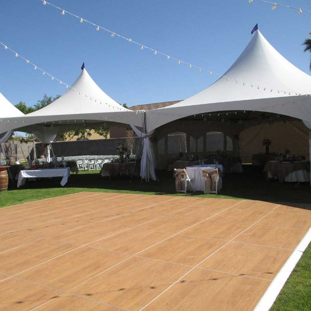 Landscape view of a large wooden 24' x 30' dance floor setup in front of three wedding tents.