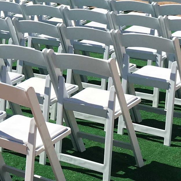 Green rental turf installed under white resin chairs at a wedding.