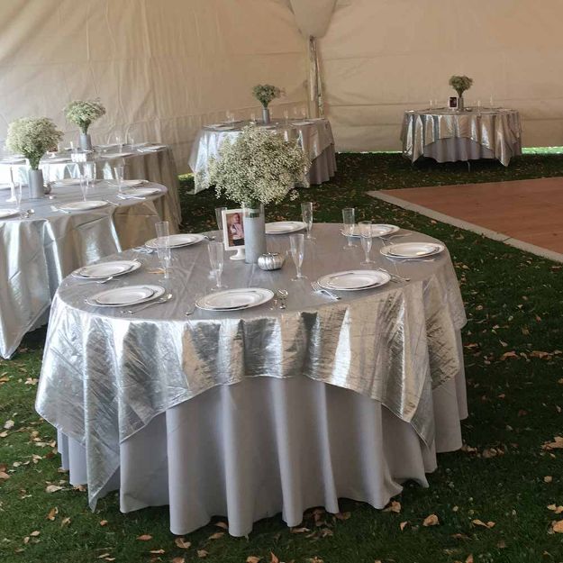 Silver decorative square linen overlay on a 60" round rental table with a white table cloth.