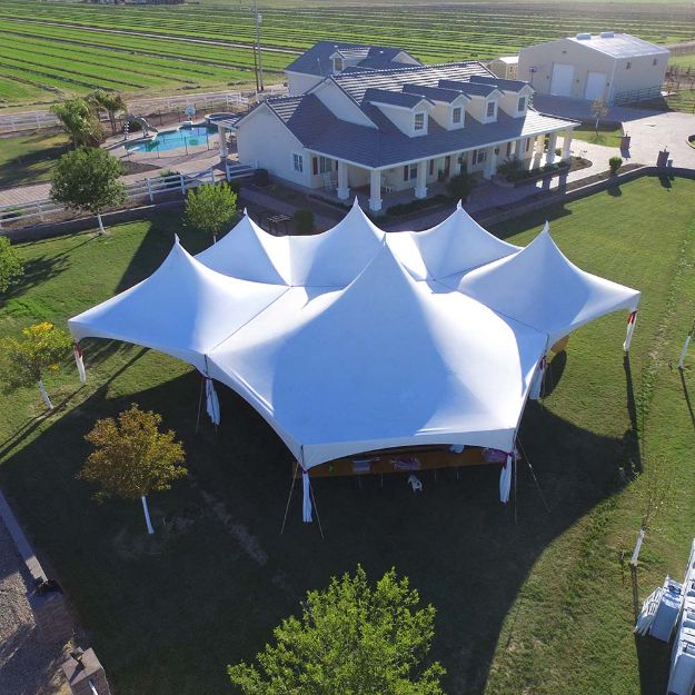 Aerial view of a rural backyard with a 170 Guest Hexagon Wedding Tent rental package erected on the lawn.