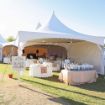 Wedding reception with decorated guest tables under a Hexagon 125 Tent with a welcome to guests sign in the foreground.