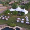 Backyard wedding reception with a Hexagon 125 rental tent, outdoor lighting and a swimming pool in the foreground.