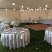 Decorated guest tables under canopy globe lighting with a dance floor setup inside a Hexagon 100 wedding tent.
