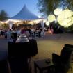 Outdoor wedding reception in progress with globe and twinkle lighting on a Hexagon 100 wedding tent package.
