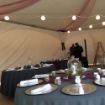 Decorated guest tables under a Hexagon 60 wedding tent with a DJ setting up his equipment in the background.