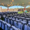 Backyard wedding with the ceremony chairs covered with white and blue cloth lined up under a Hexagon wedding tent.