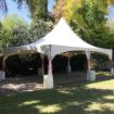 A lush backyard with green trees and lawn set the stage for an elegant white 20' x 30' rental wedding tent.