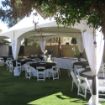 Backyard party package with guest tables, white resin chairs, black and white linens under a 20' x 40' tent canopy.