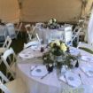 Flower centerpieces, place settings and gift bags used to decorate guest tables under a 20' x 50' Rectangle wedding tent.