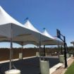 A 20' x 50' Rectangular tent canopy erected on a backyard basketball court with water barrels used for support.