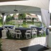 32 Guest backyard tent rental package set up with round tables, black table linens and white resin chairs next to a rural lake.