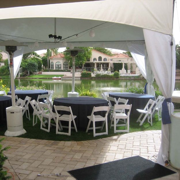 32 Guest backyard tent rental package set up with round tables, black table linens and white resin chairs next to a rural lake.