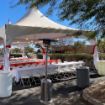 48 Guest backyard tent rental package set up with rectangle tables, black table linens and white plastic chairs with a patio heater in the foreground.