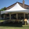 Backyard tent rental package for 48 guests with rectangle tables and white chairs set up on a back lawn.