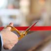 Corporate executive cutting a red ribbon with a pair of brass ribbon cutting scissors.
