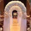 Multiple wedding arches setup down the center isle of a church with flowers and sheer material decorations.